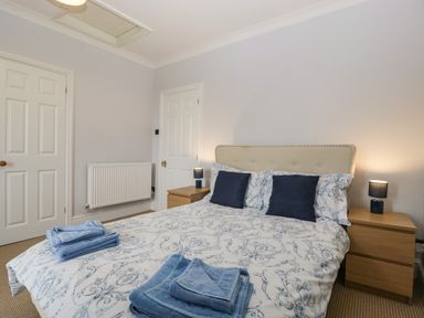 A bedroom with a bed with patterned bedding and blue cushions and towels on the bed at Moors Farm in Littledean