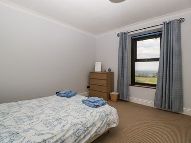 A bedroom with a bed covered in patterned bedding a wooden chest of drawers and a window with curtains at Moors Farm in Littledean