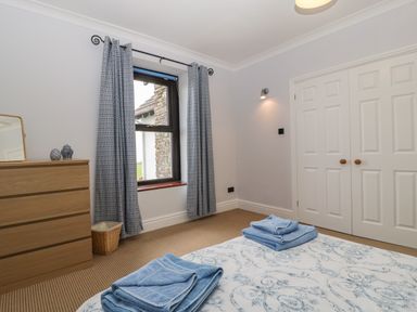 A bedroom with a bed with blue towels on it a wooden dresser with decorative items and a window with patterned curtains at Moors Farm in Littledean