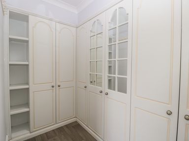 A corner with built in white wardrobes and shelves with mirrored doors at Moors Farm in Littledean