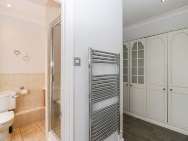 A bathroom with a toilet and shower next to a wardrobe area with white cabinets and a wall-mounted chrome towel radiator at Moors Farm in Littledean