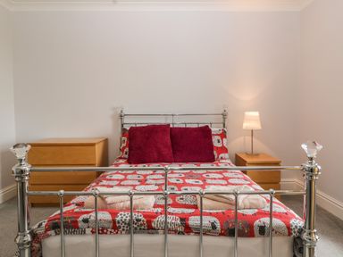 A bedroom with a metal bed frame a red patterned bedspread two purple pillows two wooden bedside tables and a lamp at Moors Farm in Littledean