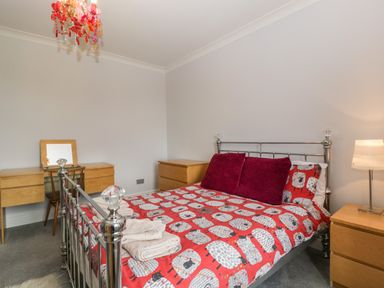 A bedroom with a metal bed frame red patterned bedding wooden dressers a wooden desk with mirror and red chandelier at Moors Farm Littledean