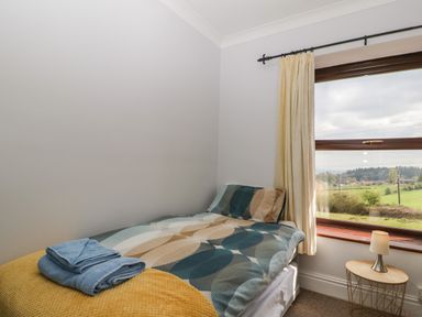 A small bedroom with a single bed next to a window and a round side table with a lamp at Moors Farm in Littledean