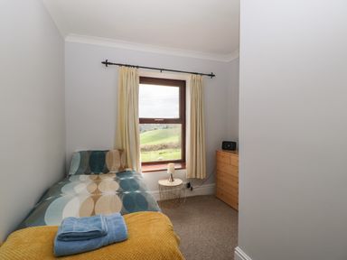 A bedroom with a bed with patterned bedding a small side table with a lamp a chest of drawers and a window with beige curtains at Moors Farm in Littledean