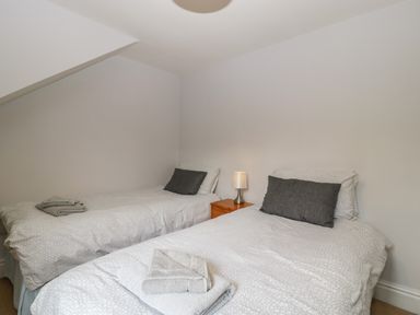 A bedroom with two single beds with gray and white bedding gray pillows and towels on the beds with a wooden nightstand and lamp between the beds at Moors Farm in Littledean