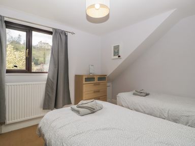 A bedroom with two single beds a wooden chest of drawers a window with grey curtains and a ceiling light at Moors Farm in Littledean