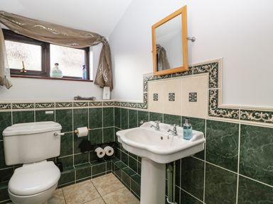 A bathroom with a toilet sink mirror and window with curtain at Moors Farm in Littledean