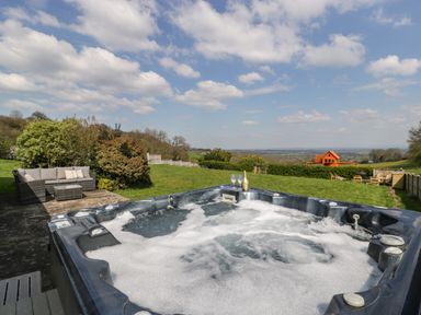 An outdoor hot tub with foam on the water in a garden with lawn seating and a wooden playhouse in the distance at Moors Farm in Littledean