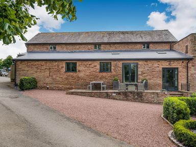 A stone building with multiple black windows and doors a gravel driveway and some outdoor seating at Teal Barn Annexe in St Weonards