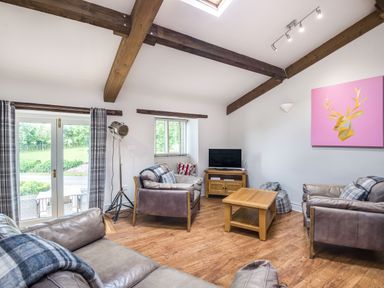 A sitting room with leather sofas a wooden coffee table a TV on a wooden stand and a pink deer artwork on the wall at Teal Barn Annexe in St Weonards