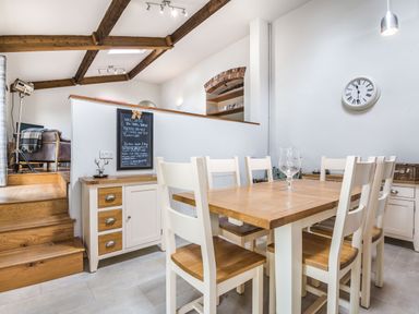 A dining area with a wooden table and chairs near stairs and a wall clock at Teal Barn Annexe in St Weonards