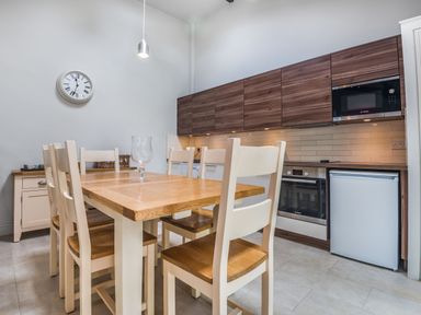 A kitchen with wooden dining table and chairs white cabinets and wall clock at Teal Barn Annexe in St Weonards