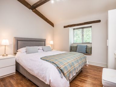 A bedroom with a double bed table lamps wooden floor and a window seat at Teal Barn Annexe St Weonards