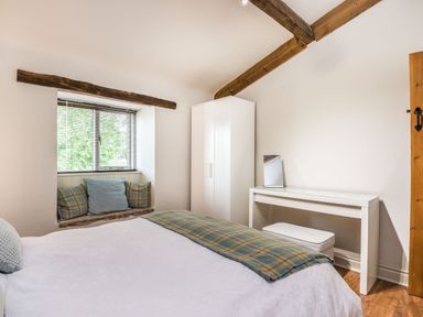 A bedroom with a bed a window seat with cushions a white wardrobe and a white dressing table at Teal Barn Annexe in St Weonards