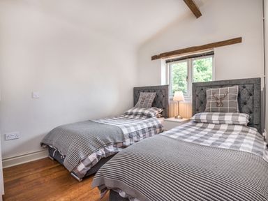 A bedroom with two single beds a bedside table with a lamp and a window at Teal Barn Annexe in St Weonards