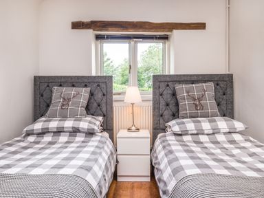 A bedroom with two single beds separated by a white nightstand and a lamp at Teal Barn Annexe in St Weonards