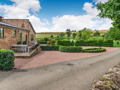 An exterior view of a stone house with a patio table and benches beside a gravel driveway and landscaped garden at Teal Barn Annexe in St Weonards