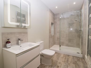 A bathroom with a sink, toilet, illuminated mirror, shower area with glass door, and towel radiator at Teal Barn Annexe in St Weonards