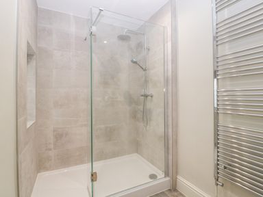 A bathroom with a glass shower enclosure a rainfall showerhead a handheld shower and a chrome towel radiator at Teal Barn Annexe in St Weonards