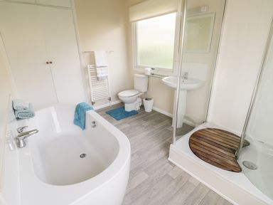 A bathroom with a bathtub a shower with a wooden mat a toilet a sink and towels at Middle Hivron in Bleddfa