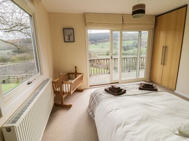 A bedroom with a bed folded towels a wooden crib a wardrobe sliding glass doors and a window with a countryside view at Middle Hivron in Bleddfa