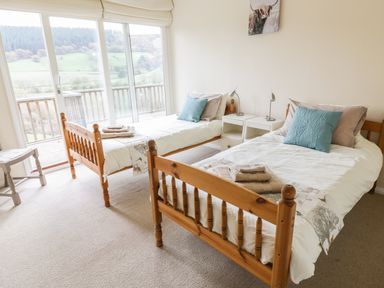 A bedroom with two wooden single beds a side table lamps and a sliding glass door leading to a balcony at Middle Hivron in Bleddfa