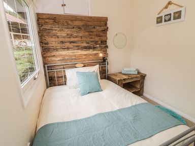 A bedroom with a bed with blue and white bedding a wooden headboard a wooden side table a round mirror and a decorative wall hanging at Middle Hivron in Bleddfa