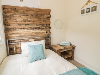 A bedroom with a bed with a wooden headboard a wooden side table with folded towels a round wall mirror and heart decorations on the wall at Middle Hivron in Bleddfa