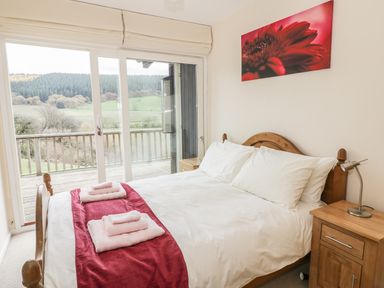 A bedroom with a wooden bed and bedside tables facing sliding glass doors and a view of trees and hills at Middle Hivron in Bleddfa