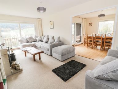 A living room with a gray sectional sofa a wooden coffee table a fireplace and an adjacent dining area with a wooden table and chairs at Middle Hivron in Bleddfa