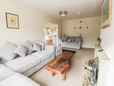 A living room with grey sofas a wooden coffee table a wall clock and a fireplace at Middle Hivron in Bleddfa