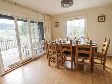 A dining room with a wooden table set for a meal and wooden chairs near sliding glass doors at Middle Hivron in Bleddfa