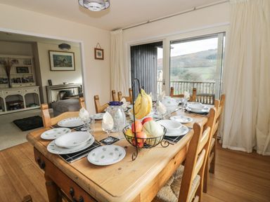A dining room with wooden table and chairs set with plates glasses and fruit basket next to sliding glass doors with a view at Middle Hivron in Bleddfa