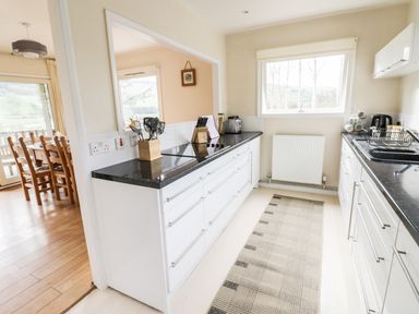 A kitchen with white cabinets black countertops kitchen utensils and a dining area visible through an open wall at Middle Hivron in Bleddfa