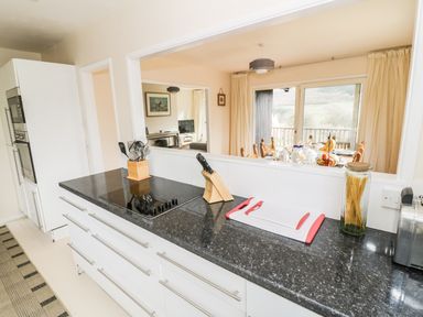 A kitchen with a black countertop stove a knife block and utensils overlooking a dining area through a pass-through window at Middle Hivron in Bleddfa