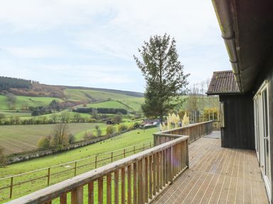 A wooden deck with railing overlooking green fields and hills at Middle Hivron in Bleddfa