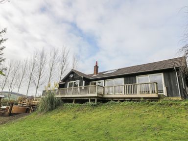 A house with a wooden deck and railing on a grassy slope with bare trees in the background at Middle Hivron in Bleddfa