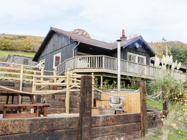 A wooden cabin with a deck and outdoor hot tub near a picnic table at Middle Hivron in Bleddfa