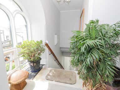 A stairwell area with potted plants and a wooden stool near arched windows at Capel Mawr in Llanrug near Llanberis