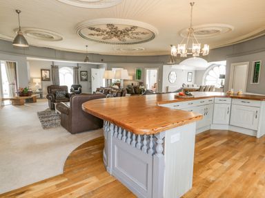 A large open plan room with a curved wooden kitchen counter several brown leather sofas a dining table and decorative ceiling at Capel Mawr Llanrug near Llanberis