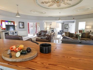 A living room with various seating arrangements and a wooden counter with chopped vegetables and a saucepan at Capel Mawr Llanrug near Llanberis
