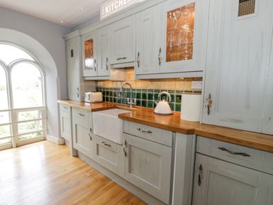 A kitchen with wooden countertops a white sink cabinets and a large window at Capel Mawr in Llanrug near Llanberis
