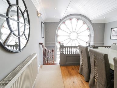 A hallway with a round window at the end a staircase on the left and a dining area with chairs on the right at Capel Mawr in Llanrug near Llanberis