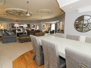 A large living and dining room with gray dining chairs a white table sofas armchairs and pendant lights at Capel Mawr in Llanrug near Llanberis