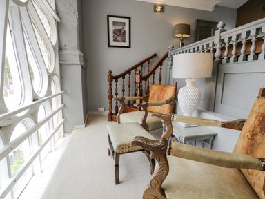 A sitting area with carved wooden chairs a lamp and a picture on the wall by a staircase at Capel Mawr in Llanrug near Llanberis