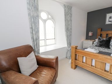 A bedroom with a wooden bed a brown leather armchair and a window with patterned curtains at Capel Mawr in Llanrug near Llanberis