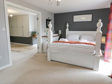 A bedroom with a white wooden bed and striped bedding and a bathroom area visible through an open door at Capel Mawr in Llanrug near Llanberis