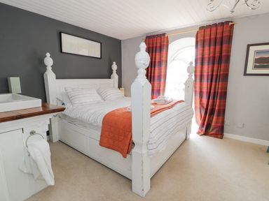 A bedroom with a white wooden bed orange blanket striped bedding and red plaid curtains at Capel Mawr in Llanrug near Llanberis