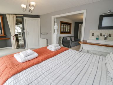 A bedroom with a bed with folded towels on an orange blanket and a view into a living area with a grey sofa at Capel Mawr in Llanrug near Llanberis